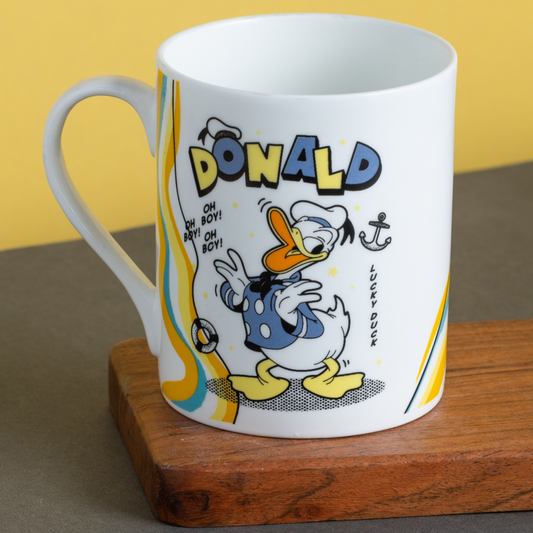 White mug with Donald Duck design on a wooden block against a yellow background
