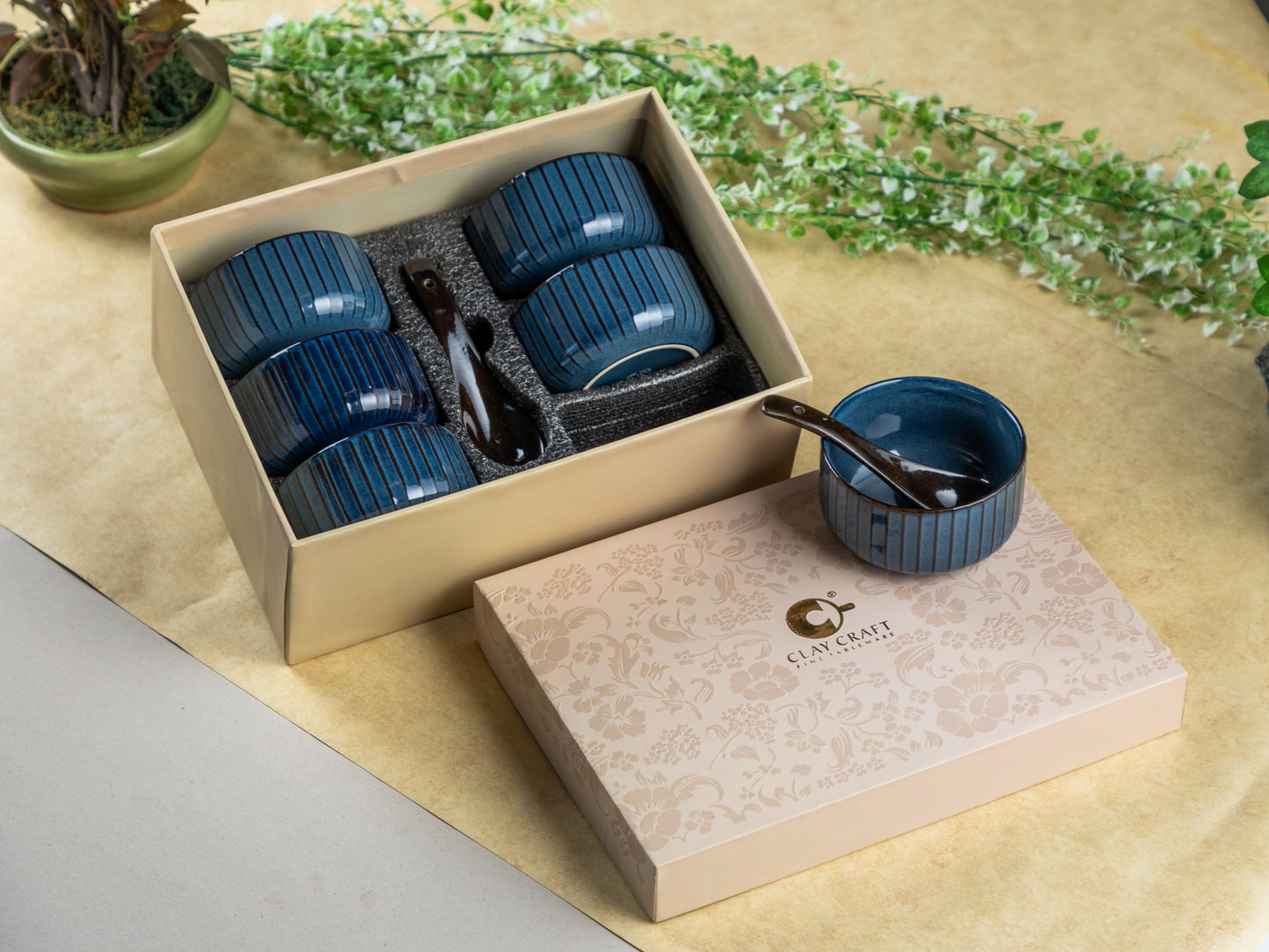Set of blue ceramic cups with a spoon in a beige box on a light surface with greenery.