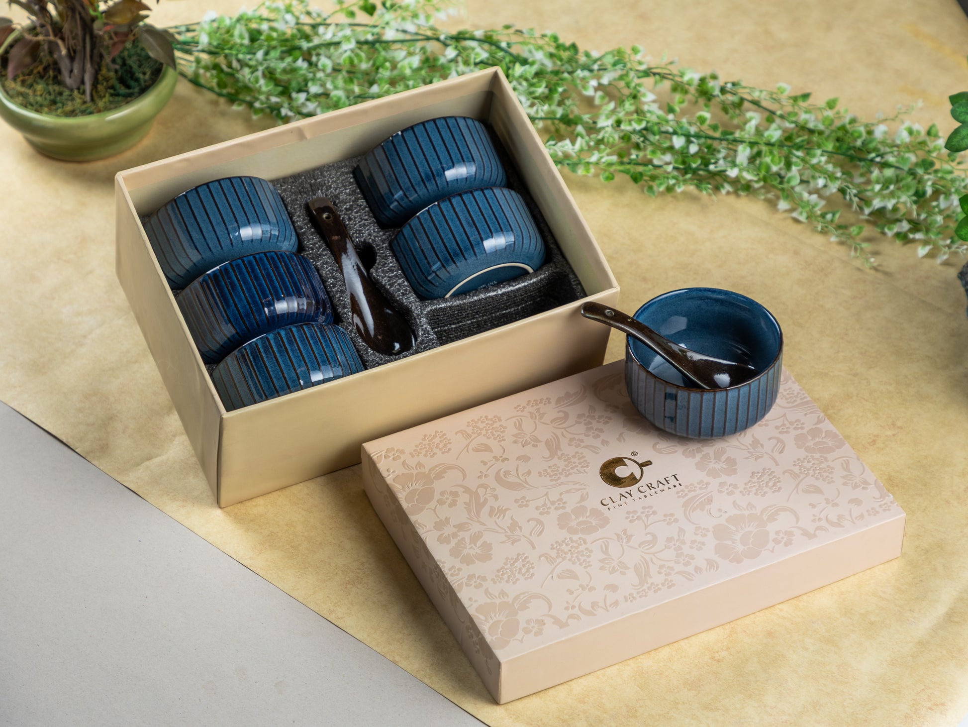 Set of blue ceramic cups with a spoon in a beige box on a light surface with greenery.